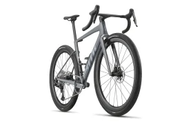 Una BMC Kaius 01 gris mate con manillar rebajado, neumáticos gruesos y frenos de disco se muestra desde un ángulo lateral trasero sobre un fondo blanco: una bicicleta rápida y actual.