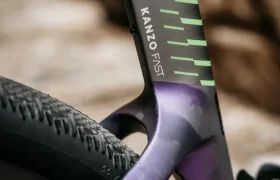 Primer plano del cuadro y la rueda trasera de una bicicleta Ridley Kanzo Fast 2.0, con el logotipo «KANZO FAST» y líneas gráficas verdes sobre un cuadro negro mate y morado, que resaltan su diseño aerodinámico y su compatibilidad con neumáticos de 58 mm para un rendimiento óptimo.