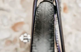 Primer plano del neumático trasero y el cuadro de una Ridley Kanzo Fast 2.0, con un muro de piedra al fondo, en el que destacan el diseño aerodinámico, el marcado dibujo del neumático y la estructura robusta, equipada con neumáticos de 58 mm.