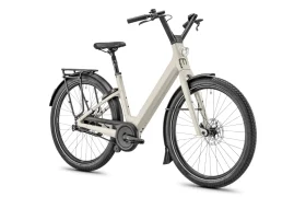 Una bicicleta eléctrica de cuadro bajo de color beige, la Moustache Lundi 27, con faro delantero, portaequipajes trasero y guardabarros negros —perfecta para explorar la ciudad—, representada sobre un fondo blanco.