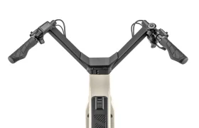 Vista superior del manillar de una bicicleta eléctrica «Moustache Lundi 27», con pantalla digital y mandos en los puños, montado en un cuadro de color beige: ideal para moverse por la ciudad con estilo y comodidad.
