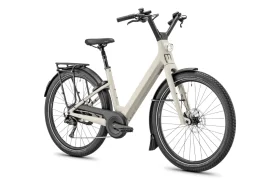 Una bicicleta eléctrica Moustache Lundi 27 de color beige, con cuadro abierto, diseñada para la ciudad, que cuenta con guardabarros delanteros y traseros, un portaequipajes trasero, luz delantera y manillar ergonómico, mostrada sobre un fondo blanco.