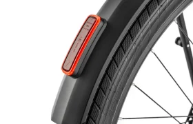 Primer plano del guardabarros trasero de una bicicleta «Moustache Lundi 27» con una luz trasera LED roja incorporada y parte de una rueda negra con la banda de rodadura y los radios visibles, ideal para moverse por la ciudad.