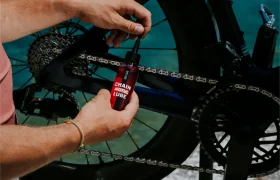 Una persona aplica lubricante para cadenas a la cadena de una bicicleta con un frasco pequeño, centrándose en el mantenimiento del sistema de transmisión de la bicicleta.