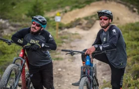Dos ciclistas, con casco y gafas de sol, se detienen con sus bicicletas de montaña Peugeot Cycles en un sendero de tierra rodeado de vegetación, mostrando la nueva gama de bicicletas perfectas para los aventureros.