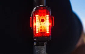 Primer plano de una luz trasera LED roja de bicicleta iluminada y montada en la tija del sillín de una bicicleta, con el sistema Radar React de Lezyne, con un fondo borroso.