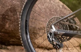 Primer plano de la rueda trasera de una bicicleta de montaña, el cassette y el desviador, con una gran roca al fondo.