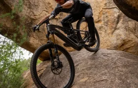 Una persona que lleva casco y gafas de sol baja en bicicleta de montaña por una gran pendiente rocosa en un entorno natural rocoso.