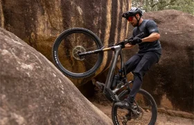 Una persona que lleva casco y gafas de sol sube en bicicleta de montaña por una pendiente rocosa y empinada, levantando la rueda delantera del suelo.