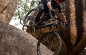 Un ciclista de montaña, con todo el equipo puesto, desciende por una empinada pared rocosa entre grandes cantos rodados, haciendo gala de su control y equilibrio.