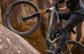 Primer plano de una persona que sube en una bicicleta de montaña con suspensión total por una pendiente empinada y rocosa, en el que se ven las ruedas y el cuadro de la bicicleta, así como parte de las piernas y los brazos del ciclista.