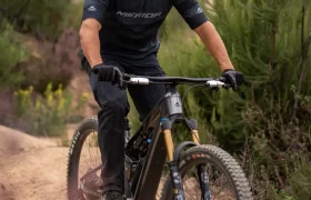 Una persona que lleva casco y gafas de sol va en bicicleta de montaña por un sendero de tierra rodeado de vegetación.