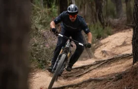 Una persona que lleva casco baja en bicicleta de montaña por un sendero de tierra que atraviesa una zona boscosa, inclinándose en una curva.