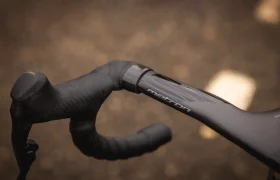 Primer plano del manillar y la potencia integrados de una bicicleta de carretera MMR Aelion negra, con la marca "medron", sobre un fondo marrón difuminado.