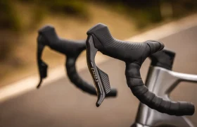 Primer plano del manillar negro con manetas de freno y cambio SRAM RED en una bicicleta de carretera MMR Aelion SL, sobre un fondo borroso al aire libre.