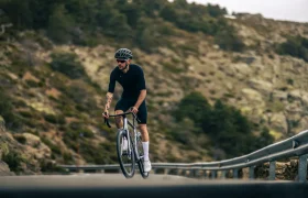 Un ciclista con atuendo negro y casco conduce una MMR Aelion cuesta arriba por una sinuosa carretera de montaña con guardarraíles y árboles de fondo, mostrando el verdadero espíritu bici total.