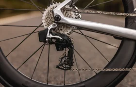 Primer plano de la rueda trasera de una bici total MMR Aelion, destacando el casete, la cadena y el cambio trasero en una carretera asfaltada lisa con un toque de acento asturiano en cada detalle.