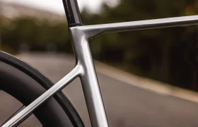 Primer plano de un moderno cuadro de bicicleta, destacando la unión entre el tubo de sillín y el tubo superior de la elegante MMR Aelion SL, con una carretera borrosa y vegetación de fondo.