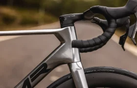 Primer plano del manillar, el cuadro y la rueda delantera de una bicicleta MMR Aelion en una carretera asfaltada vacía con un fondo natural asturiano difuminado.