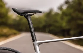 Primer plano del sillín de una bicicleta MMR Aelion, la tija del sillín y parte del cuadro con una carretera exterior difuminada y árboles al fondo-un toque de bici total con acento asturiano.