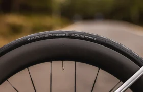 Primer plano de una rueda de bicicleta MMR Aelion con un neumático Hutchinson Racing Lab Blackbird, con una carretera borrosa y vegetación de fondo.