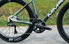 Primer plano de una transmisión de bicicleta de carretera, con ruedas DT Swiss, plato Shimano Ultegra y cuadro MMR Aelion, con un aire de bici total sobre un fondo de hierba difuminado.