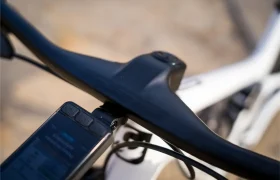 Primer plano del manillar y la potencia de una bicicleta, en el que destaca un manillar integrado de carbono FSA NS SIC, con un dispositivo electrónico acoplado que muestra información, todo ello montado en un cuadro blanco de bicicleta de montaña.