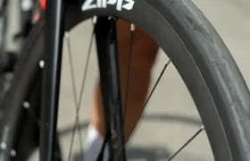 Primer plano de la rueda delantera de una bicicleta de carretera con la marca «Zipp», equipada con un neumático Schwalbe Pro One Aero, en el que se aprecia parte de la horquilla y el disco de freno sobre una superficie asfaltada.