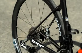 Primer plano de la rueda trasera, el cassette y la transmisión de una bicicleta de carretera negra equipada con un neumático Schwalbe Pro One sobre una superficie de asfalto.
