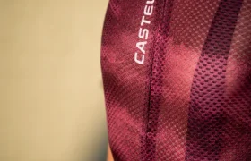 Persona que lleva un maillot de ciclismo Castelli de color granate y unos culotes Climber’s A/C, mostrada desde los hombros hasta la cintura, de pie sobre un fondo liso de color beige para un máximo rendimiento térmico.
