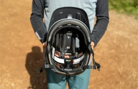 Una persona vestida con ropa de montaña sostiene frente a la cámara un casco de bicicleta negro POC Cularis Pure, mostrando claramente el acolchado interior, las correas y los detalles de la visera.