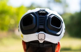Una persona que lleva un casco de ciclismo POC blanco con dos grandes rejillas de ventilación negras, vista desde atrás, al aire libre en un día soleado. Perfecto para salidas por grava o carretera, este casco polivalente ofrece versatilidad y seguridad allá donde te lleve tu viaje.