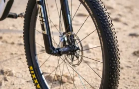 Primer plano de la rueda delantera y la horquilla de suspensión de una bicicleta de montaña, equipada con neumáticos Maxxis y ruedas FSA, en un sendero arenoso al aire libre para un control total.