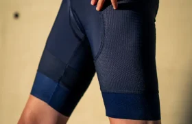 Una persona que lleva unos culotes de ciclismo Castelli Climber’s A/C de color azul marino y una camiseta de malla granate posa con una mano en la cadera ante un fondo liso, preparada para dar el máximo rendimiento en condiciones de calor.