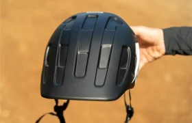 Una persona sostiene un casco de bicicleta POC Cularis Pure negro, con múltiples rejillas de ventilación y una correa ajustable, que se muestra al aire libre sobre un fondo marrón difuminado. El casco cuenta con viseras Sol para una mayor protección y comodidad durante los recorridos bajo el sol.