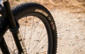Primer plano de la rueda delantera y el neumático negros de una bicicleta de montaña en un camino de tierra, equipada con ruedas FSA para un control total, con hierba seca al fondo.