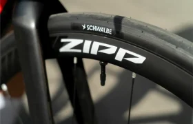 Primer plano de una rueda de bicicleta en el que se aprecia una llanta Zipp y un neumático Schwalbe Pro One Aero, con parte de la horquilla y los radios a la vista.