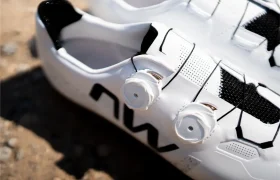Primer plano de un par de zapatillas de ciclismo blancas con detalles en negro y cierres de dial, colocadas sobre una superficie rugosa al aire libre. Las Northwave Extreme X destacan en esta imagen, lo que refleja su diseño de gama alta y su reconocida versatilidad para los ciclistas que buscan tanto rendimiento como estilo.