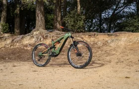 Una bicicleta de montaña verde y negra con detalles en naranja, equipada con el Polini E-P3+ MX para lograr esa potencia italiana característica, está estacionada en un camino de tierra en una zona boscosa.