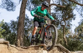 Una persona con un maillot verde y un casco recorre en bicicleta de montaña un terreno rocoso en un entorno forestal, impulsada por la impresionante Polini E-P3+ MX, que muestra pura potencia italiana.