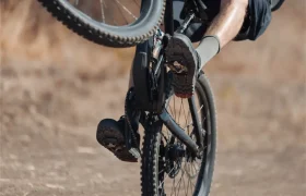 Una persona que va en bicicleta de montaña equipada con pedales Shimano DEORE XT hace un «wheelie» en un camino de tierra, con solo la rueda trasera tocando el suelo.