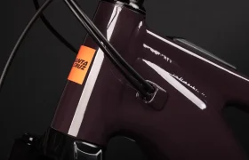 Primer plano de un cuadro de bicicleta Santa Cruz Vala AL aluminio de color púrpura oscuro que muestra el cableado interno y el logotipo de Santa Cruz de color naranja brillante sobre fondo negro.