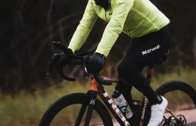 Un ciclista con casco y linterna frontal, chaqueta de neón y pantalones negros conduce una bicicleta de carretera Trek por una carretera asfaltada, canalizando el espíritu de Kilian Jornet mientras abordan diferentes estados de elevación.