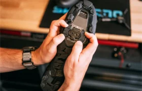 Una persona ajusta una cala en la suela de sus zapatillas de ciclismo gravel Shimano RX710, utilizando las manos, con herramientas y una alfombrilla visibles al fondo.