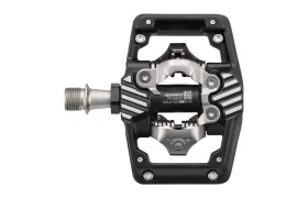 Un pedal de bicicleta Shimano DEORE XT, en negro y plateado, con una estructura rectangular abierta y un eje metálico, diseñado para ofrecer un rendimiento SPD XC Gravel, mostrado sobre un fondo blanco.