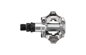 Un pedal de bicicleta sin clip Shimano DEORE XT, de color plateado y negro, con cuerpo metálico y mecanismo de resorte, visto de perfil sobre un fondo blanco; ideal para el ciclismo de montaña Trail o para el ciclismo de grava (XC Gravel) con pedales SPD.