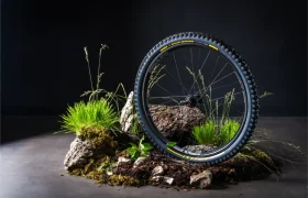 Una rueda de bicicleta de montaña equipada con neumáticos Pirelli Scorpion MTB aparece en posición vertical entre rocas, hierba y tierra, sobre un fondo oscuro.