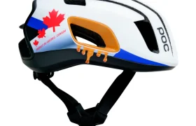 Casco de bicicleta blanco con correas negras, decorado con una hoja de arce roja, la inscripción «Proudly of Quebec, Canada» y detalles gráficos de color naranja. Se aprecia el nombre de la marca «POC».
