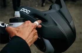 Una persona sostiene un casco integral negro POC Barocon Carbon mientras aprieta una botella de agua por encima de él, lo que transmite una sensación dinámica de descenso.