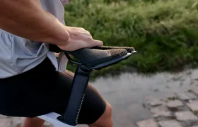 Una persona con ropa de ciclista ajusta un sillín PRO Stealth 3D en una bicicleta negra, de pie sobre un camino empedrado con hierba al fondo.